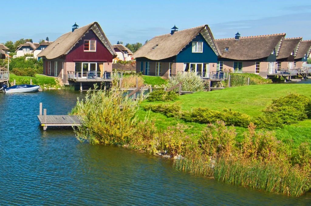 Eine Reihe von bunten Häusern mit Reetdächern am Ufer eines ruhigen Kanals an einem sonnigen Tag. Eine Reihe von bunten Häusern mit Reetdächern am Ufer eines ruhigen Kanals an einem sonnigen Tag.